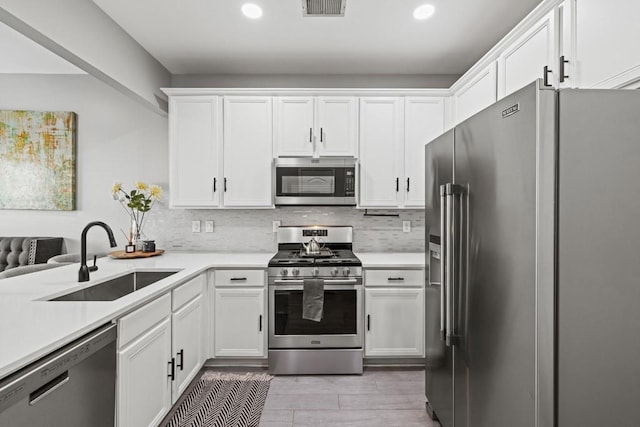 kitchen with sink, appliances with stainless steel finishes, white cabinets, decorative backsplash, and light wood-type flooring