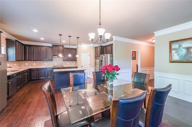 dining space featuring dark wood-style floors, a wainscoted wall, crown molding, a decorative wall, and a notable chandelier