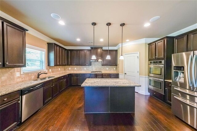 kitchen with dark wood-type flooring, decorative backsplash, appliances with stainless steel finishes, light stone countertops, and a kitchen island