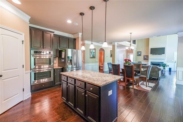 kitchen featuring pendant lighting, dark hardwood / wood-style floors, appliances with stainless steel finishes, dark brown cabinetry, and a center island