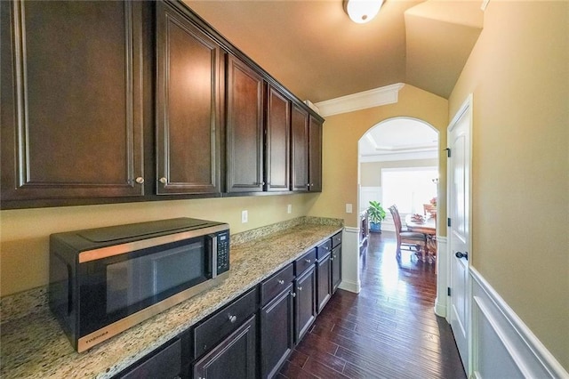 kitchen featuring arched walkways, stainless steel microwave, dark wood-style flooring, vaulted ceiling, and crown molding