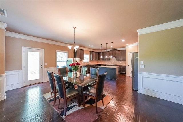 dining space with dark wood-type flooring, sink, ornamental molding, and an inviting chandelier