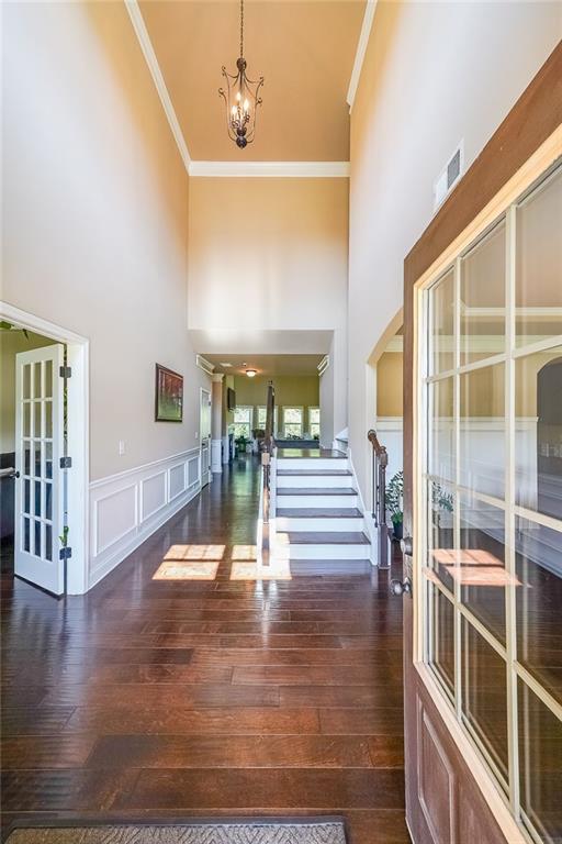 entryway with french doors, dark wood-type flooring, a high ceiling, a notable chandelier, and ornamental molding