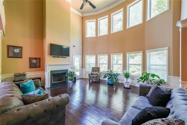 living room with ceiling fan, dark hardwood / wood-style flooring, ornamental molding, and a towering ceiling