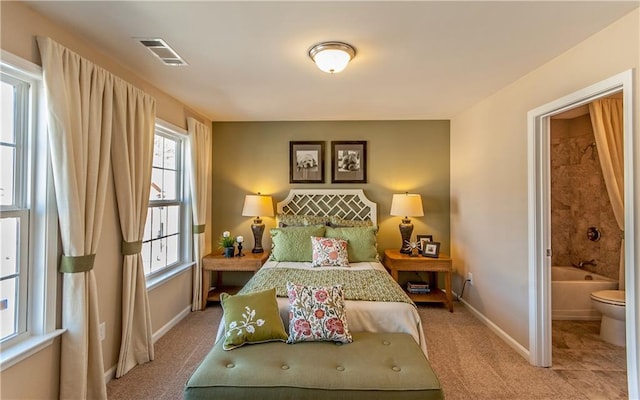 bedroom featuring baseboards, visible vents, ensuite bathroom, and light carpet