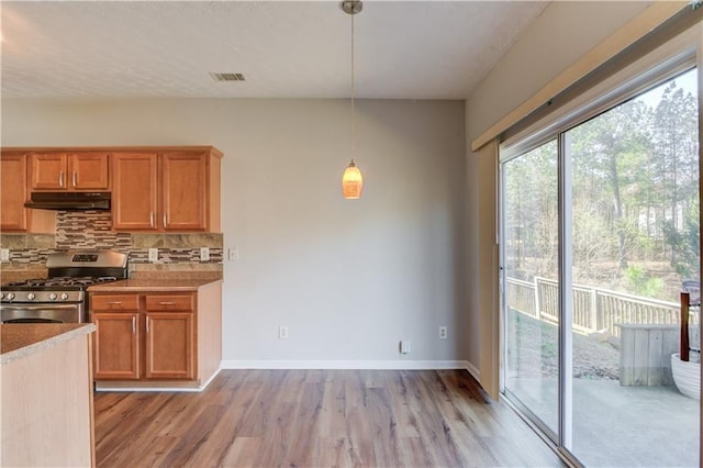 kitchen featuring under cabinet range hood, visible vents, stainless steel gas range, and tasteful backsplash