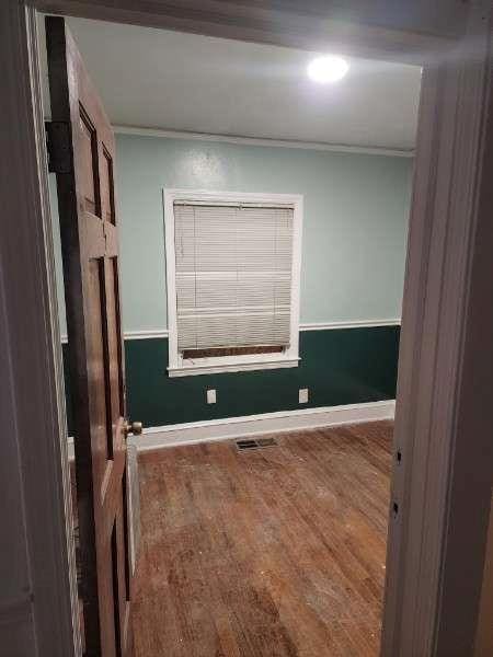 unfurnished room with wood finished floors, visible vents, baseboards, and ornamental molding