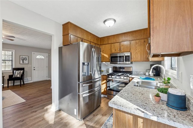 kitchen with appliances with stainless steel finishes, sink, ceiling fan, light stone counters, and light hardwood / wood-style flooring