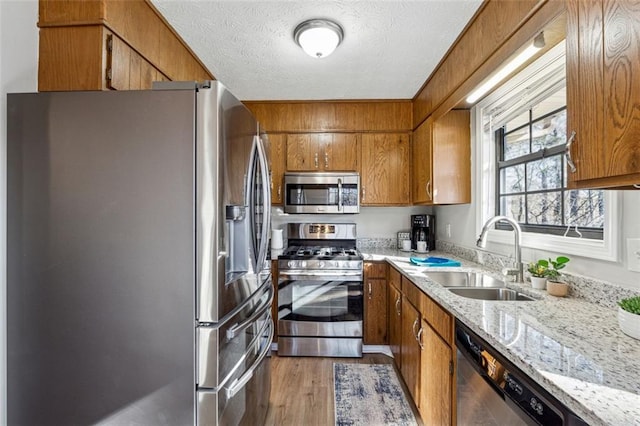 kitchen with sink, wood-type flooring, a textured ceiling, stainless steel appliances, and light stone countertops