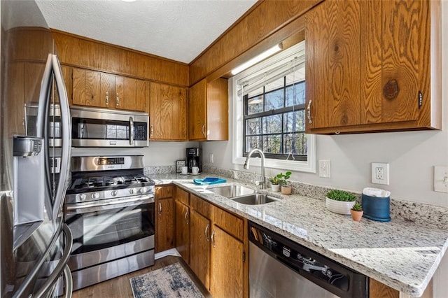 kitchen featuring appliances with stainless steel finishes, sink, dark hardwood / wood-style flooring, light stone countertops, and a textured ceiling