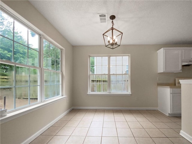 unfurnished dining area with light tile patterned flooring, a textured ceiling, and a chandelier