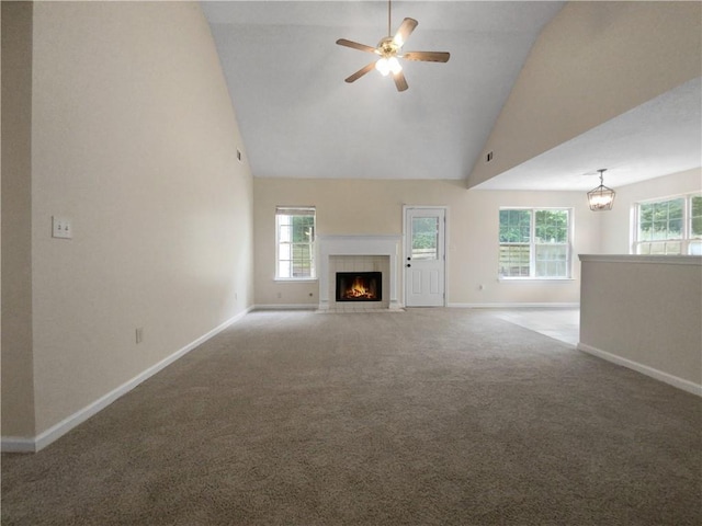 unfurnished living room featuring carpet, ceiling fan with notable chandelier, a healthy amount of sunlight, and a tiled fireplace