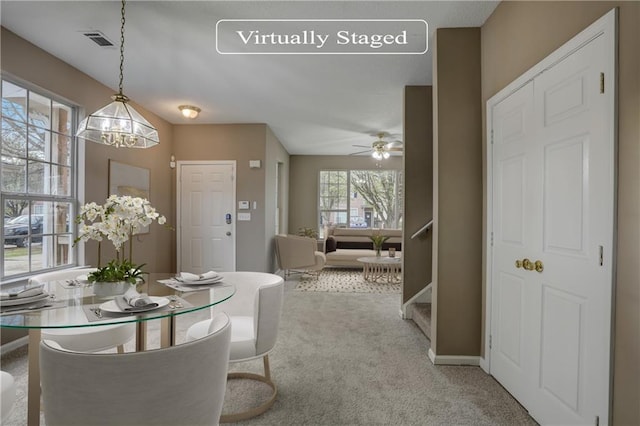 carpeted dining area with ceiling fan with notable chandelier