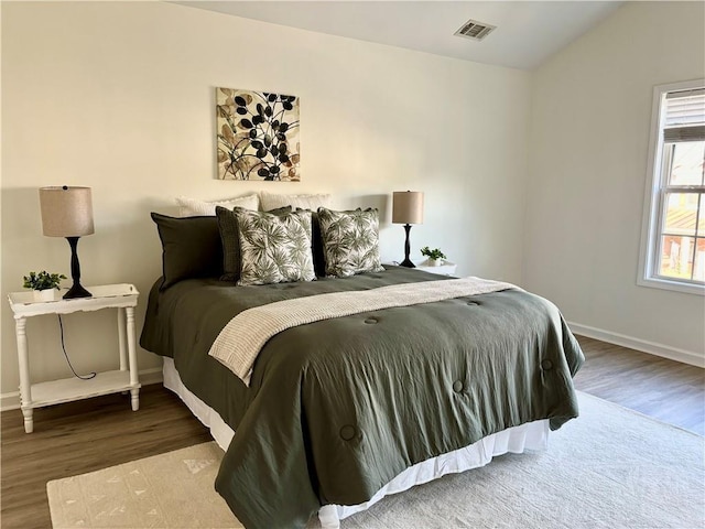 bedroom with lofted ceiling, visible vents, baseboards, and wood finished floors