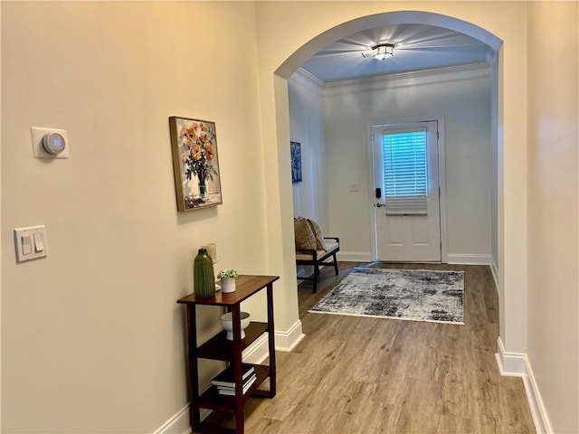 doorway featuring arched walkways, baseboards, wood finished floors, and crown molding