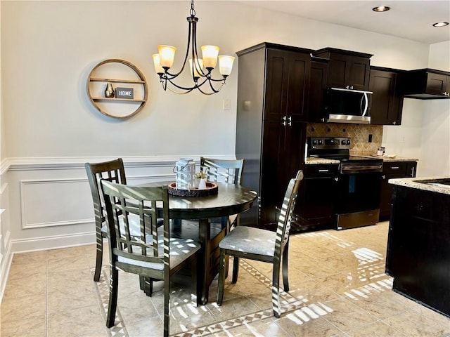 dining space with light tile patterned floors, wainscoting, a decorative wall, and an inviting chandelier