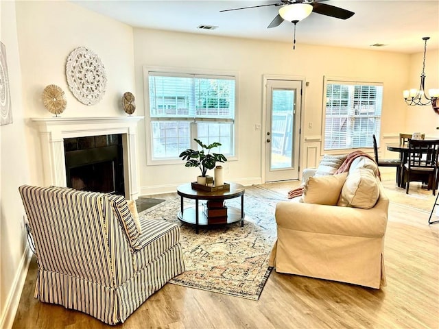 interior space with baseboards, visible vents, a tile fireplace, wood finished floors, and ceiling fan with notable chandelier