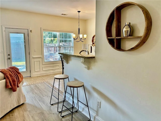 entryway featuring a decorative wall, a notable chandelier, visible vents, wainscoting, and light wood-type flooring