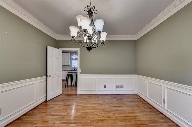 unfurnished dining area with crown molding, sink, a chandelier, and light hardwood / wood-style floors