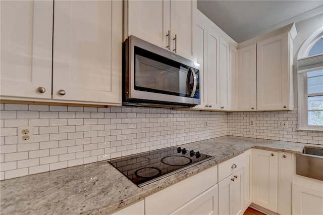 kitchen with black electric cooktop, light stone counters, white cabinetry, and tasteful backsplash