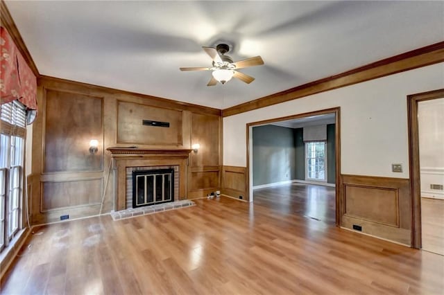 unfurnished living room featuring a brick fireplace, hardwood / wood-style flooring, crown molding, and ceiling fan