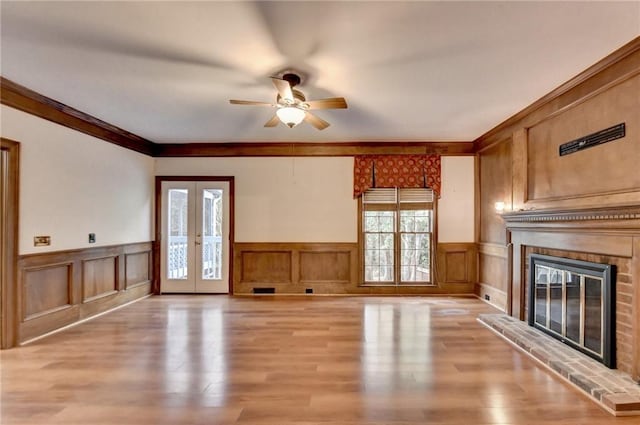 unfurnished living room featuring french doors, light wood-type flooring, a brick fireplace, and ornamental molding