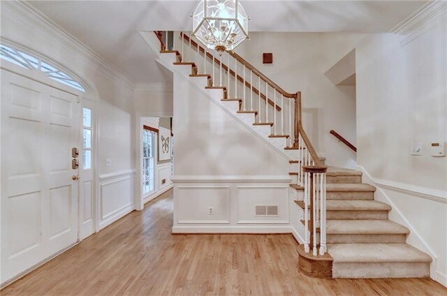 entryway with an inviting chandelier, crown molding, and light hardwood / wood-style floors