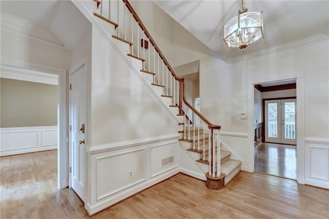 foyer featuring french doors, an inviting chandelier, light wood-type flooring, and ornamental molding