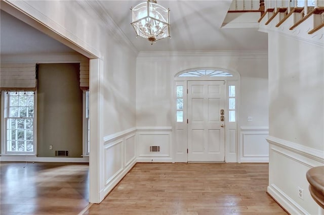 foyer entrance with crown molding, light hardwood / wood-style floors, and a chandelier