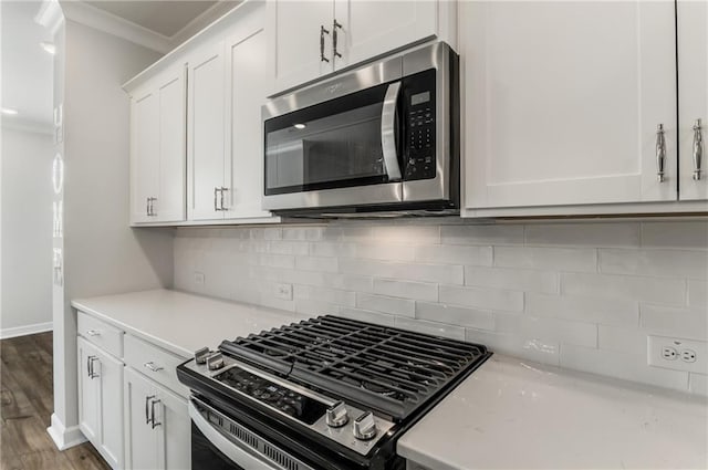 kitchen featuring stainless steel appliances, white cabinetry, ornamental molding, wood-type flooring, and decorative backsplash