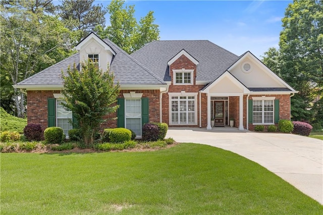 view of front facade with brick siding, a front yard, and roof with shingles
