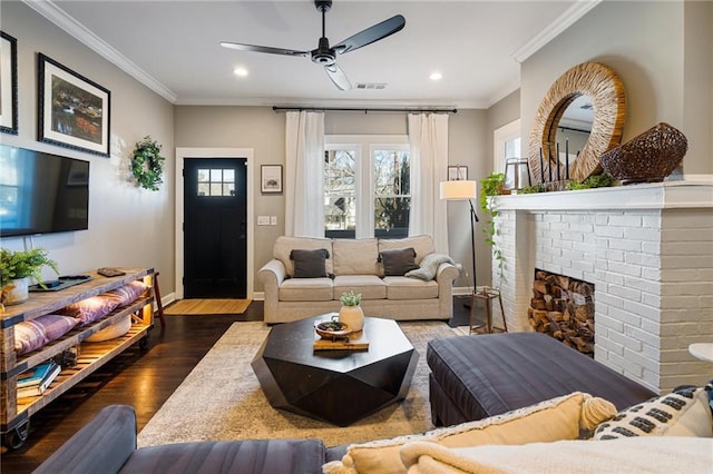 living room with crown molding, a brick fireplace, dark hardwood / wood-style floors, and ceiling fan