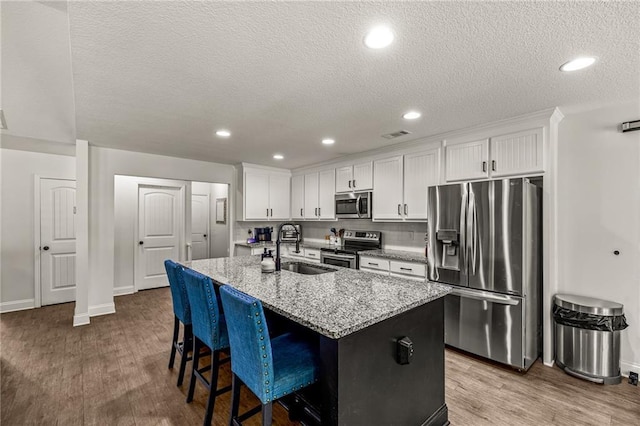 137 Evergreen Ridge Ct, Statham, GA 30666 - kitchen featuring stainless steel appliances, a sink, an island with sink, white cabinetry, and light stone counters