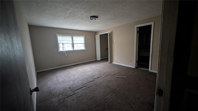 empty room featuring a textured ceiling, dark colored carpet, and baseboards