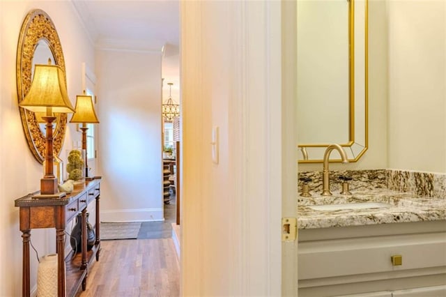 hall with crown molding, a chandelier, sink, and light wood-type flooring