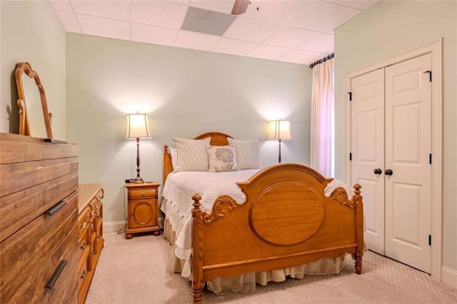 bedroom with ceiling fan, a closet, a paneled ceiling, and light carpet