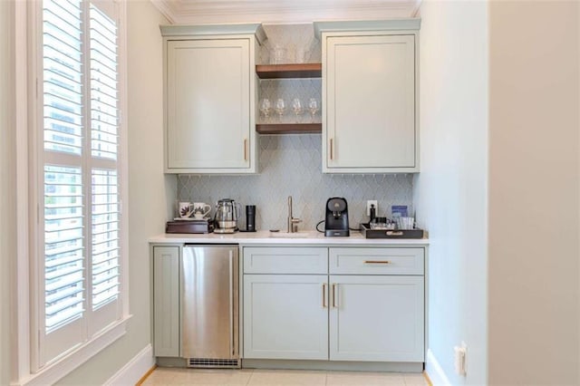 bar featuring sink, crown molding, light tile patterned floors, refrigerator, and decorative backsplash