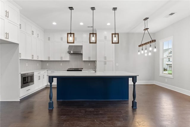 kitchen with wall chimney range hood, dark hardwood / wood-style flooring, tasteful backsplash, stainless steel microwave, and decorative light fixtures