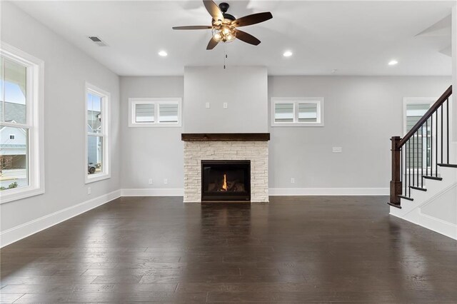 unfurnished living room featuring ceiling fan, a stone fireplace, wood-type flooring, and a healthy amount of sunlight