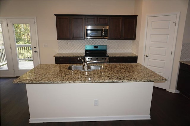 kitchen featuring appliances with stainless steel finishes, a sink, dark brown cabinetry, and light stone countertops