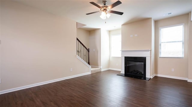 unfurnished living room featuring dark wood-type flooring, a ceiling fan, baseboards, and stairs