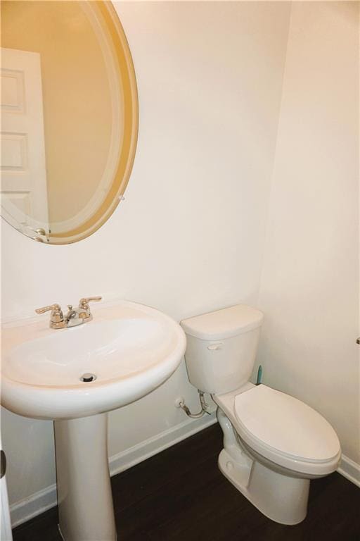 half bath with toilet, baseboards, and wood finished floors