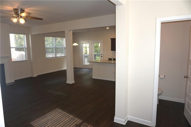 unfurnished living room with dark wood-style floors, plenty of natural light, baseboards, and a ceiling fan