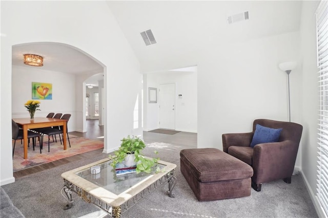 living area featuring high vaulted ceiling, arched walkways, visible vents, and baseboards