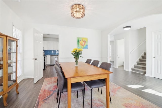 dining area with baseboards, stairway, arched walkways, and dark wood-style flooring