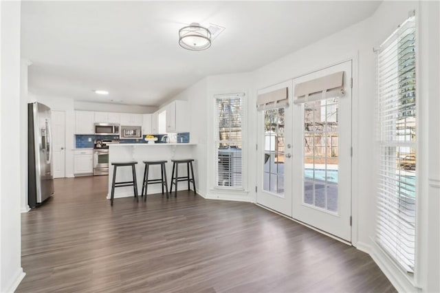 kitchen with a peninsula, dark wood finished floors, white cabinets, appliances with stainless steel finishes, and a kitchen bar