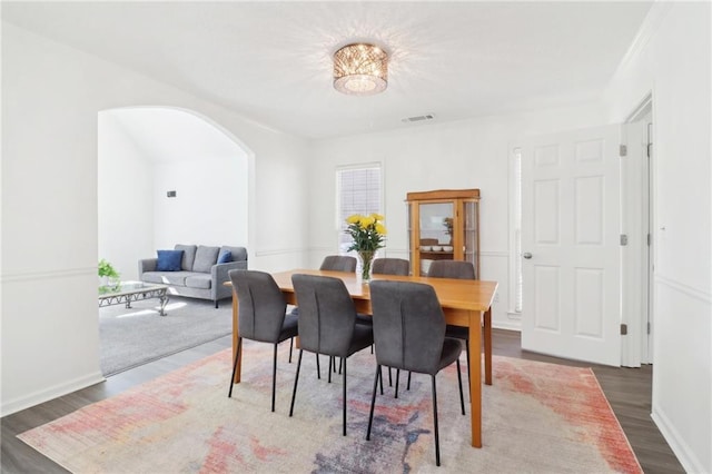 dining room featuring arched walkways, wood finished floors, visible vents, and baseboards