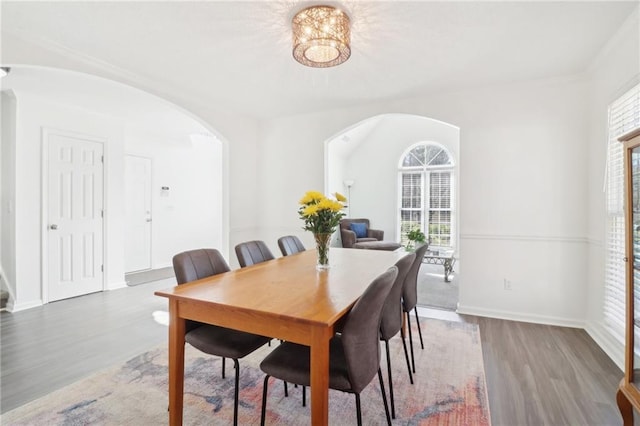 dining area with a healthy amount of sunlight, baseboards, arched walkways, and wood finished floors