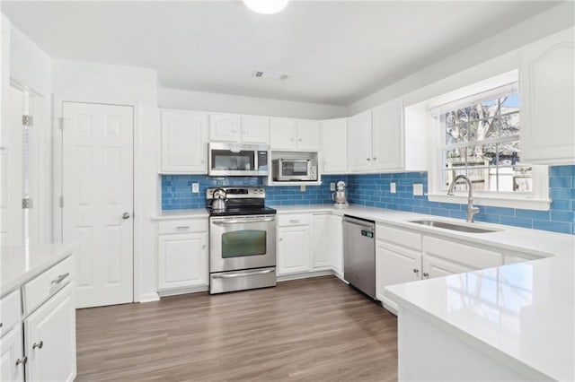 kitchen with appliances with stainless steel finishes, white cabinets, a sink, and wood finished floors