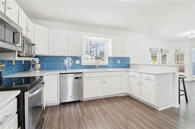 kitchen with a breakfast bar area, stainless steel appliances, a peninsula, a sink, and light wood-style floors